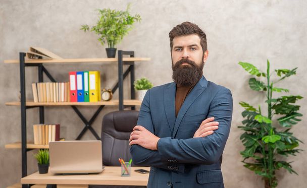 mature entrepreneur in jacket standing crossed hands at office with copy space, charisma. - Фото, изображение