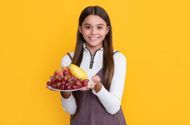 positive child hold fruit plate on yellow background. - Foto, imagen