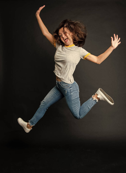 Happy cool ecstatic energetic girl jumping up midair dark background, jump. - Photo, image