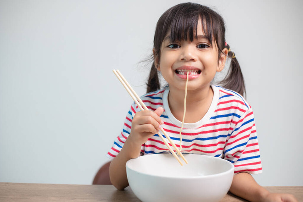 Cute Asian child girl eating delicious instant noodles at home. - Foto, Imagem