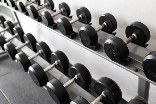 Stand with dumbbells. Sports and fitness room. Weight Training Equipment. Black dumbbell set, many dumbbells on rack in sport fitness center - Fotó, kép
