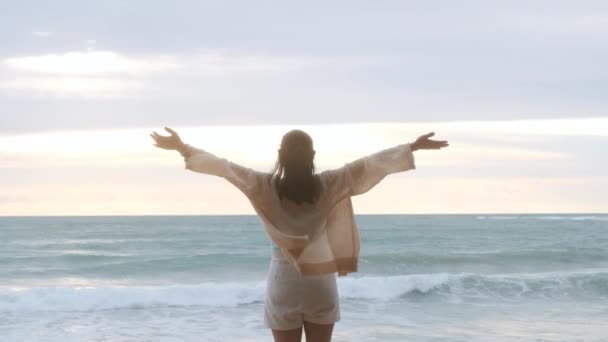 Portrait of a beautiful Asian woman smiling relaxing on the beach. A young woman strolling along the sea looking at the big waves and strong winds. Concept of relaxation and travel on vacation. - Metraje, vídeo