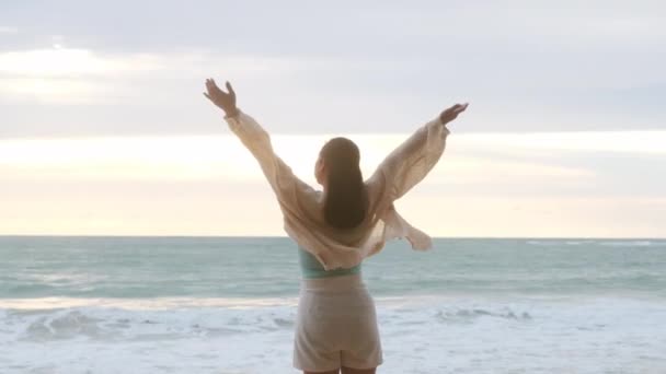 Πορτρέτο μιας όμορφης Ασιάτισσας που χαμογελάει χαλαρώνοντας στην παραλία. Μια νεαρή γυναίκα που περπατούσε στη θάλασσα κοιτάζοντας τα μεγάλα κύματα και τους δυνατούς ανέμους. Έννοια της χαλάρωσης και των ταξιδιών στις διακοπές. - Πλάνα, βίντεο