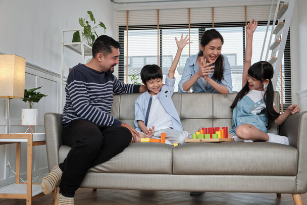 Счастливая азиатская милая тайская семья, папа, мама и маленькие дети получают удовольствие, играя с разноцветными игрушечными блоками вместе на диване в белой гостиной, веселые выходные и домашний здоровый образ жизни. - Фото, изображение