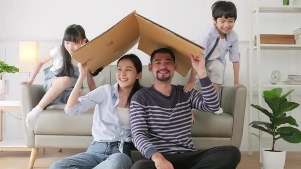 Asian Thai family, adult dad, mum, and little children happily fun playing in a white living room, built cardboard paper safety house with imagination, lovely weekend and wellbeing domestic lifestyle. - Footage, Video