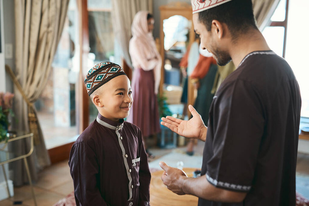 Muslim father and son talking and bonding in the living room during a religious holiday at home. Cute, smiling and happy Islamic boy listening to advice from his dad while wearing traditional outfit. - Fotoğraf, Görsel
