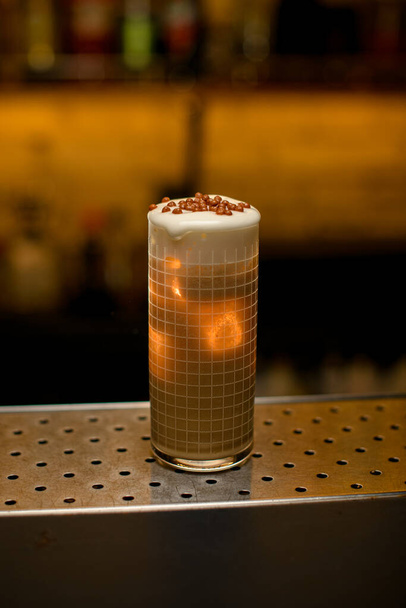 Close-up of beautiful glass with grid pattern full of cocktail garnished with whipped cream and chocolate balls - Fotó, kép