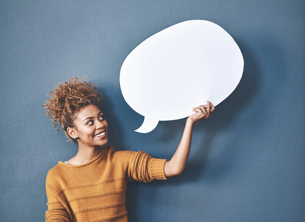 Young woman holding a speech bubble against a grey background in a studio. Portrait of a casual, happy and smiling female holding copy space empty shape for social media, chat and voice or message - Photo, Image