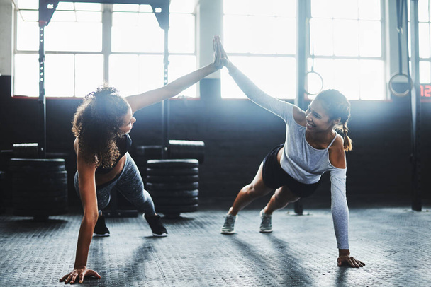 Мотивация все меняет. Две молодые женщины дают друг другу пять, делая отжимания в спортзале - Фото, изображение