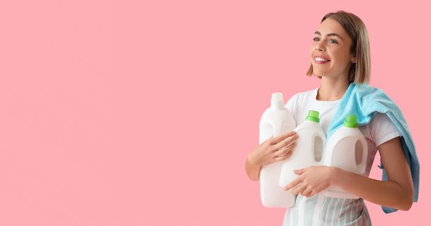 Pretty young woman holding bottles of detergent on pink background with space for text - Fotografie, Obrázek