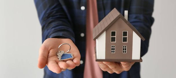 Real estate agent holding house model and key on light background, closeup - Foto, Imagem