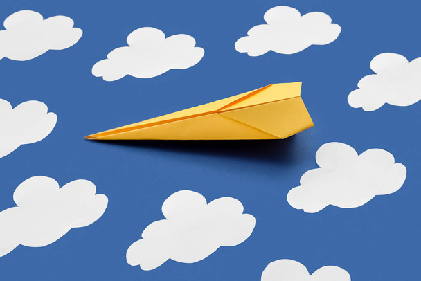Yellow paper plane and clouds on blue background - Fotó, kép