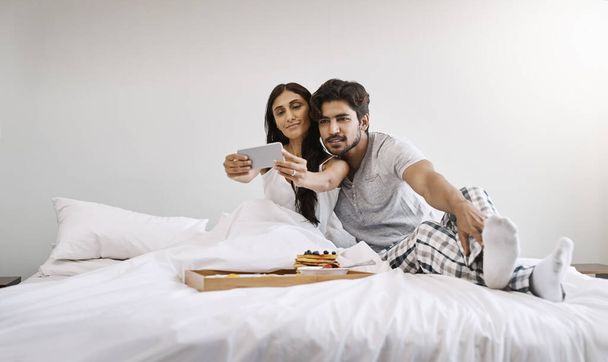 Early morning selfies. Full length shot of an affectionate young couple taking selfies while having breakfast in bed - Foto, Imagem