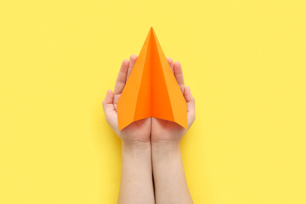 Woman with orange paper plane on yellow background - Foto, afbeelding