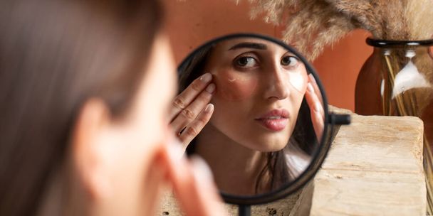 Reflection of woman applying under-eye patch at dressing table closeup. Professional facial skin care. Antiaging and refreshing cosmetic products - Фото, изображение