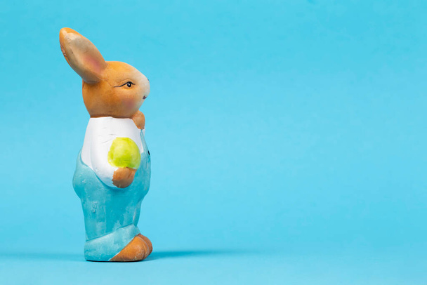 Фигура плюшевого пасхального кролика с яйцом на синем фоне. Пасхальная карточка. - Фото, изображение