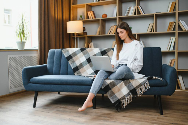 Portrait of a young happy female freelancer sitting on the couch and working on project, watching movie on laptop, studying, blogging, resting and chatting online. High quality photo. - Foto, imagen