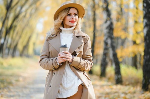 Young beautiful woman holding cup with coffee in the autumn park - Foto, Imagen
