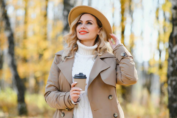 Pretty young woman with coffee cup in the autumn park. - Foto, immagini