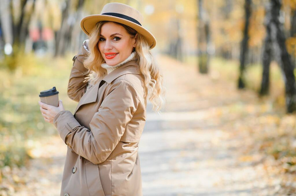 Young beautiful woman holding cup with coffee in the autumn park - Foto, Imagem