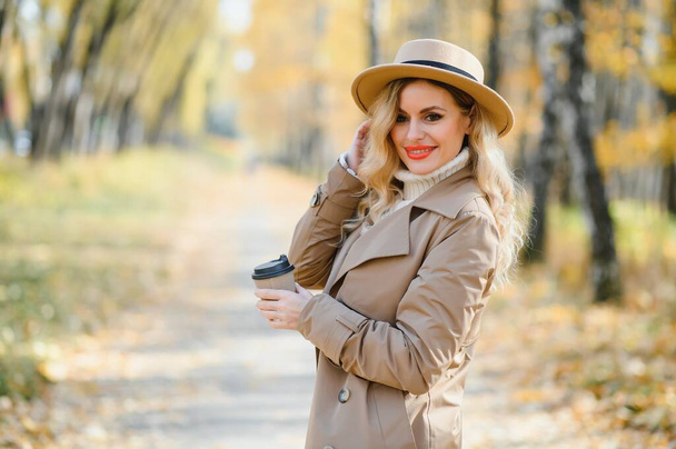 Pretty young woman with coffee cup in the autumn park. - Fotoğraf, Görsel