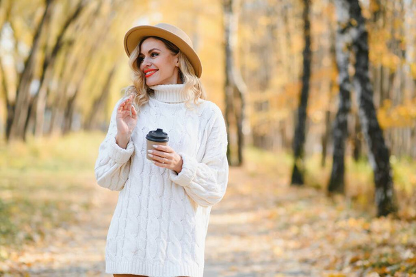 Pretty young woman with coffee cup in the autumn park. - Φωτογραφία, εικόνα