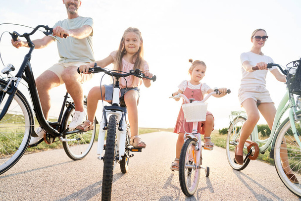 Сім'я з чотирьох кавказьких людей, що сидять на велосипедах на сільській дорозі
  - Фото, зображення