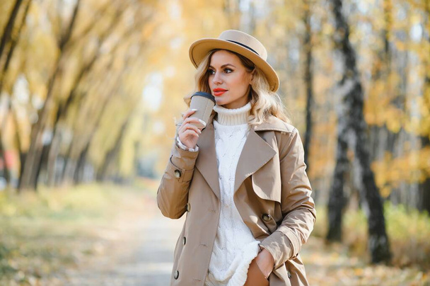 Young beautiful woman holding cup with coffee in the autumn park - Фото, зображення