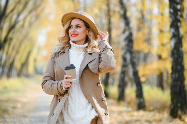 Pretty young woman with coffee cup in the autumn park. - Photo, Image