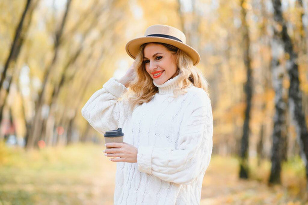 Young beautiful woman holding cup with coffee in the autumn park - Fotografie, Obrázek