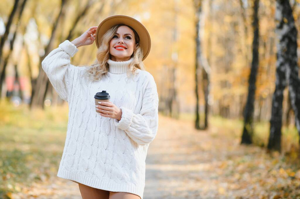 Young beautiful woman holding cup with coffee in the autumn park - Foto, imagen