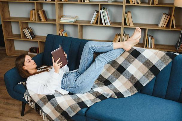 Закройте расслабленную девочку, используя смартфон, лежащий на диване в гостиной дома
 - Фото, изображение