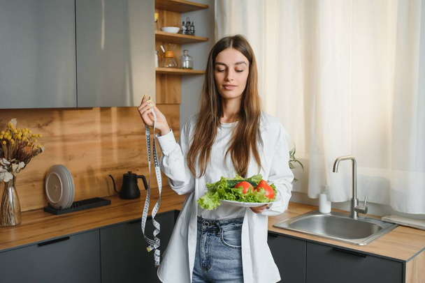 Happy young woman preparing salad in kitchen. Healthy diet. - 写真・画像