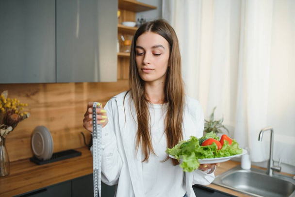 Happy young woman preparing salad in kitchen. Healthy diet. - Fotó, kép