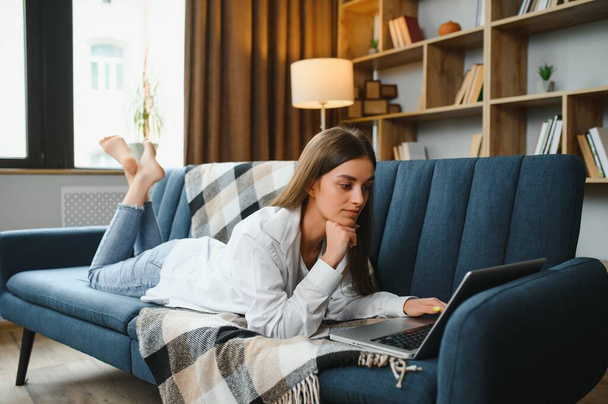 Young woman lying on couch with laptop - Foto, Bild