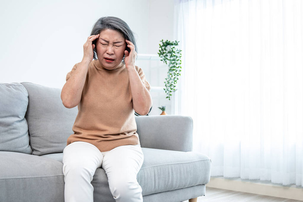 An agonizing senior woman with a headache, compress her temple with both hands at her contented living room. Senior health, nursing home, caretaker service. - Foto, imagen