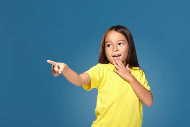 Χαριτωμένο κορίτσι δείχνει το δάχτυλό της σε μπλε φόντο - Φωτογραφία, εικόνα