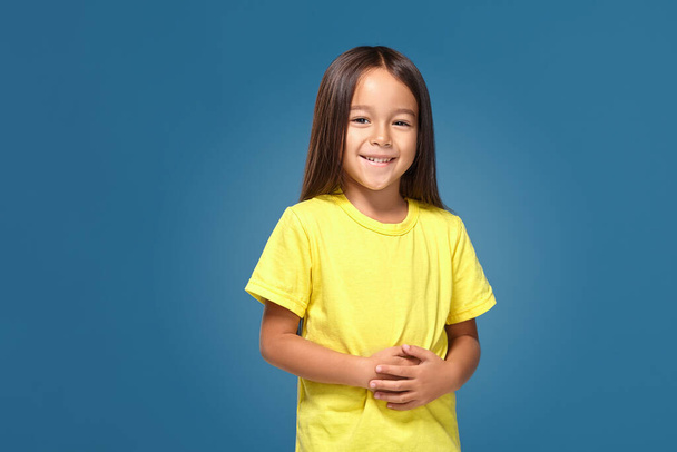 Маленька дівчинка в жовтій футболці посміхається на синьому фоні
 - Фото, зображення