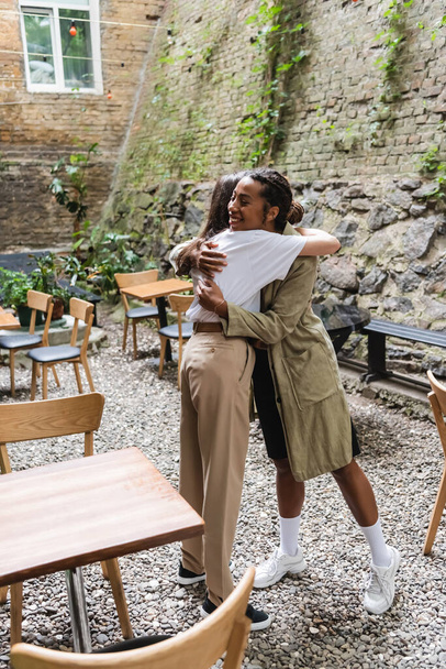 African american woman hugging friend on terrace of cafe  - Foto, afbeelding