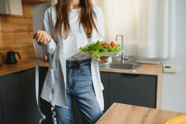 Happy young woman preparing salad in kitchen. Healthy diet. - Fotó, kép