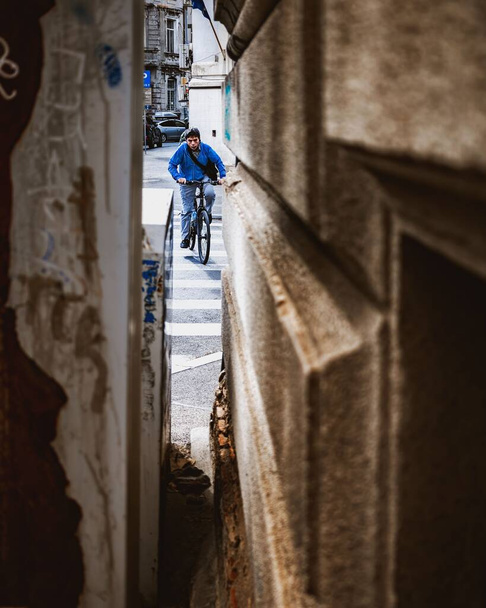 A man in a blue shirt visible from the small hole between buildings riding a bicycle on the streets of Bucharest - Zdjęcie, obraz