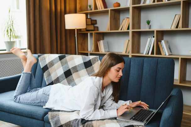 Freelancer working on laptop at home laying on comfortable beige sofa - Valokuva, kuva