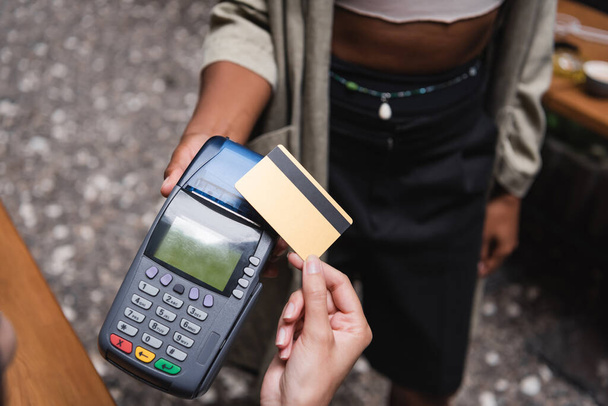 Cropped view of client paying with credit card near african american waitress in outdoor cafe  - Фото, изображение