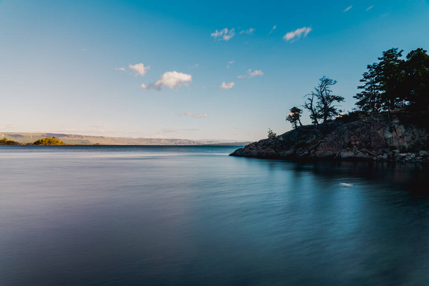 A beautiful view of a lake captured near trees and rocks during daylight - Photo, Image