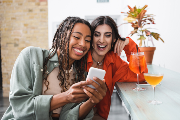 Positive multiethnic friends using smartphone near cocktails in cafe  - Foto, Imagen