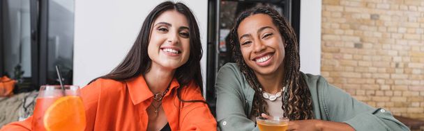 Positive interracial friends looking at camera near cocktails in cafe, banner  - Photo, Image