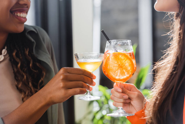 Cropped view of multiethnic girlfriends clinking cocktails in cafe  - Photo, Image
