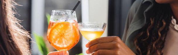 Cropped view of multiethnic girlfriends clinking cocktails in cafe, banner  - Foto, Bild