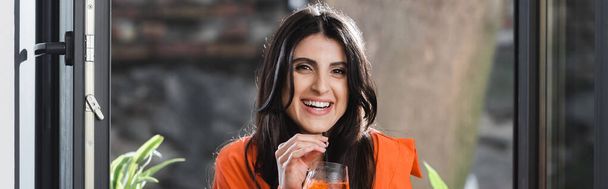 Smiling woman holding cocktail with drinking straw near window in cafe, banner  - Photo, image