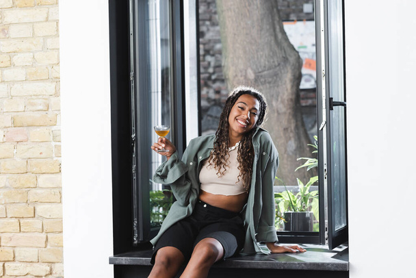 Cheerful african american woman holding cocktail near window in cafe  - Foto, Imagem